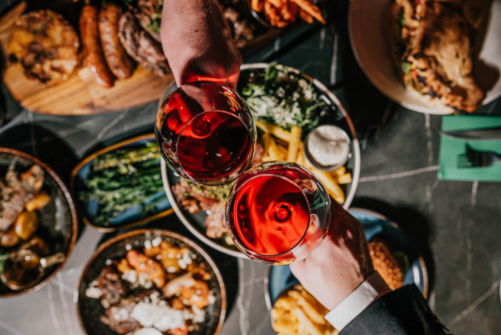 Diners raising glasses of red wine over a table of Mediterranean sharing dishes at Stripped Brasserie